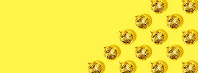 Creative Christmas pattern. Shiny gold disco balls over yellow background. Flat lay, top view. New year baubles, star sparkles. Party time. Cristmas greeting card