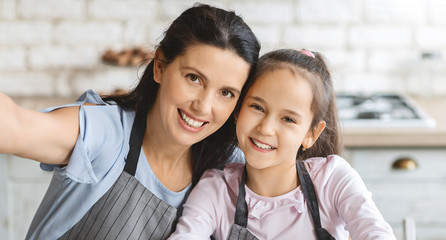Beautiful mom and her cute daughter taking selfie in kitchen