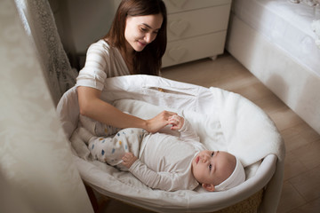 Little baby lying in crib and young mother sits about it. happy family. 