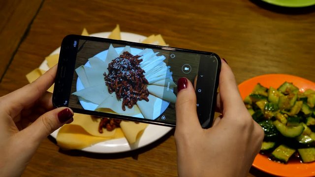 Woman make photograph of served food at Chinese restaurant, using smartphone. Customer girl take picture of Jing Jiang Rou Si meal, Beijing style shredded pork served with onions and sheets of tofu