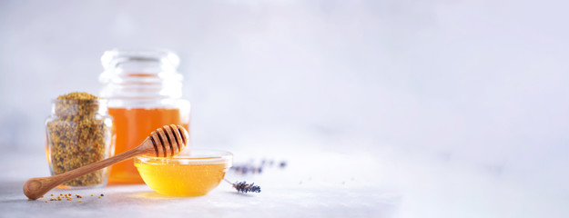 Honey products background. Honeycomb frame, bee pollen granules, honey in glass pot on grey...