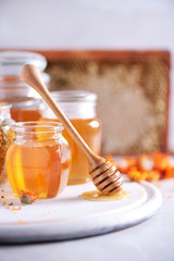 Herbal honey in jar with dipper, honeycomb, bee pollen granules, calendula flowers on grey background.