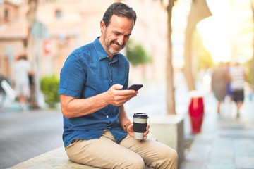 Middle age handsome businessman using smartphone drinking take away coffee smiling