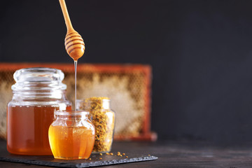 Bee pollen granules, honey jar with wooden dropper, honeycomb on dark backdrop. Copy space. Autumn...