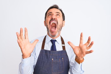 Middle age shopkeeper man wearing apron standing over isolated white background crazy and mad...