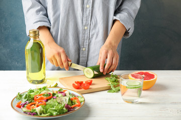 Young woman slices cucumber for salad on wooden background