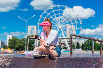Portrait of an emotional girl in a pink cap visor wearing protective gloves and rollerblades...