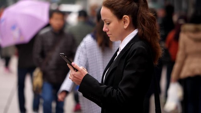 Business woman stay and look to phone, portrait shot at pedestrian street at Chinese city. Blurred background, many people walk at Nanjing Road, slow motion shot.