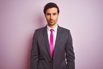 Young handsome businessman wearing suit and tie standing over isolated pink background Relaxed with serious expression on face. Simple and natural looking at the camera.