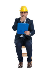 businessman with safety helmet holding his clipboard and looking terrified
