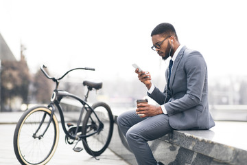 Afro businessman listening music and drinking coffee with bike nearby