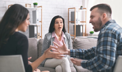 Amazed family therapist looking at mad couple arguing at session