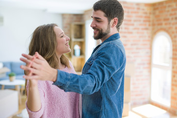 Fototapeta premium Young couple dancing celebrating moving to new apartment around cardboard boxes