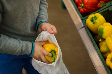 Children's hands put pepper in a bag of cotton at the supermarket. Reusable environmental shopping bag. Zero waste concept - reuse.
