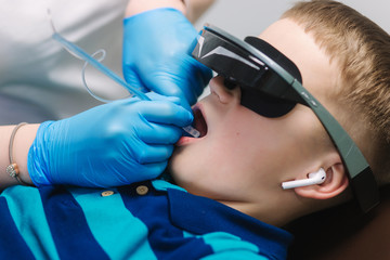 Close up of little boy sitting in dentist in vr glasses and wireless headphones while dentist make x-ray of teeth