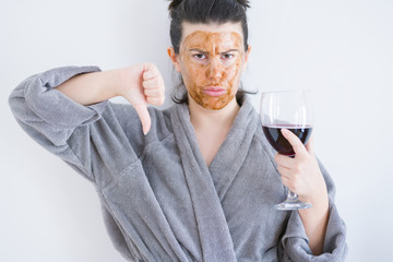 Beautiful woman wearing cosmetic facial mask as skincare treatment drinking glass of wine with angry face, negative sign showing dislike with thumbs down, rejection concept