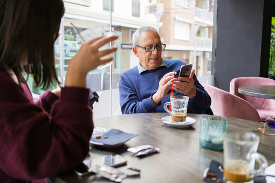 Senior man having a conversation with woman drinking coffee using smartphone and relaxing, chatting at restaurant