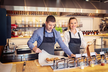 Cheerful waiters wearing apron serving takeaway food at counter in fast food restaurant