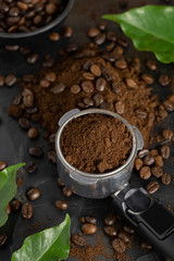 Coffee beans on Metal portafilter or Filter Holderand  and ground powder on black marble background. Top view 