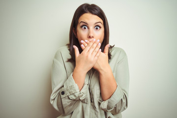 Young beautiful brunette woman wearing green shirt over isolated background shocked covering mouth with hands for mistake. Secret concept.