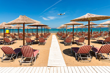 Empty beach with chairs, sunbeds, straw umbrellas, and blue sky. Mediterranean summer vacation destination, Heraklion, Crete, Greece.