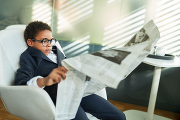 Kind als Geschäftsmann liest Zeitung im Büro