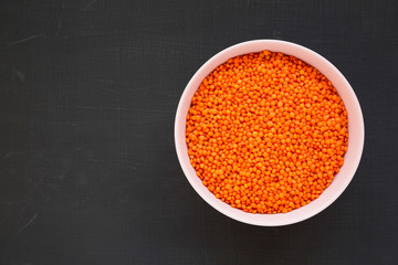 Red lentils in a pink bowl on a black background, top view. Flat lay, overhead, from above. Copy space.