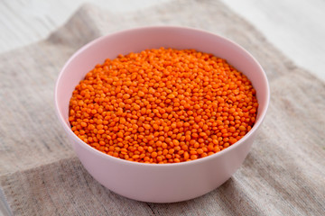 Red lentils in a pink bowl on a white wooden surface, side view. Close-up.