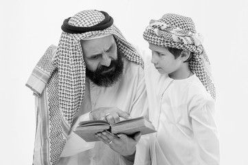 Arabic grandather and grandson reading holy book together indoors .