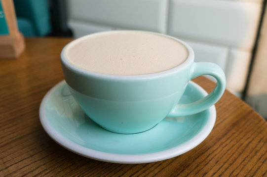 Turquoise Cup of coffee on a wooden table in the cafe. A Cup of lavender Rafe against a white brick wall
