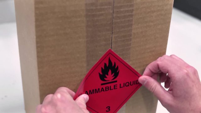 Worker Putting A Sticky Label Reading Flammable Liquid On A Cardboard Box
