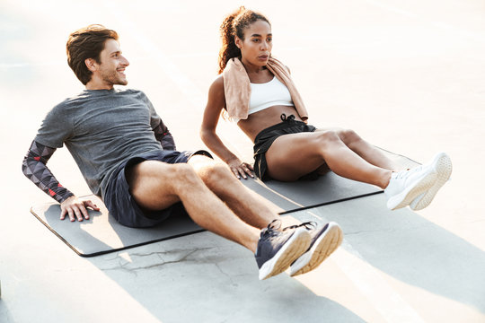 Photo of multinational young couple doing exercise on mat