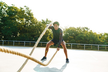 Photo of strong concentrated man doing workout with battle ropes