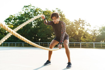 Photo of athletic masculine man doing workout with battle ropes
