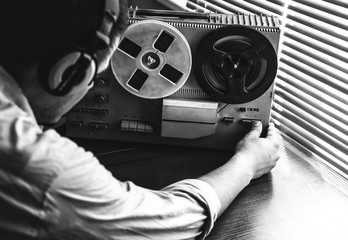 Special agent listens on the reel tape recorder. Officer wiretapping in headphones. KGB spying of conversations.  Cold war period. Black and white photo. - obrazy, fototapety, plakaty