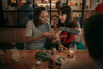 Two smiling friends sitting at a bistro table sharing food