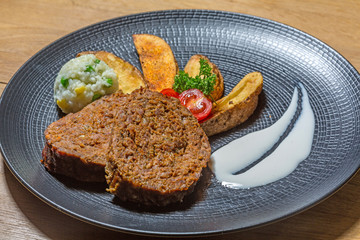 Veggie meat served on black plate with potato and rice and green peas