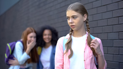 Unhappy schoolgirl standing front of laughing cruel pupils, college mocking