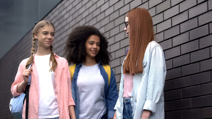 Two school pupils bullying modest red-haired teenager, pushing scared classmate