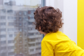 Five years old child in yellow T-shirt looking out window of high floor.