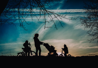 Fototapeta na wymiar mother with baby in stroller and kids on bikes walk in sunset nature