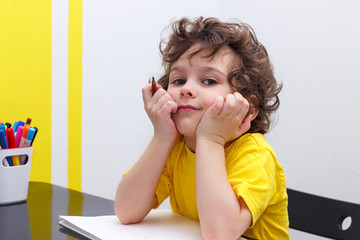 Little curly boy sits at a table, smiles, has a rest after the letter, eyes are closed.