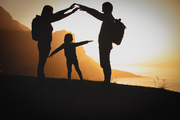 Fototapeta na wymiar happy family- mom, dad and little girl- travel in mountains at sunset