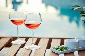 two glasses of rose wine with  olives against blue water on a pier..