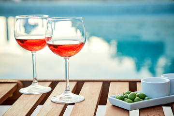 two glasses of rose wine with  olives against blue water on a pier..