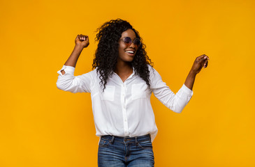 Pretty african woman with sunglasses dancing over yellow background