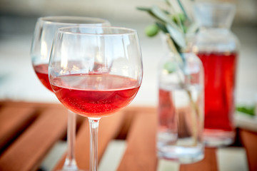 two glasses of rose wine with  olives against blue water on a pier..