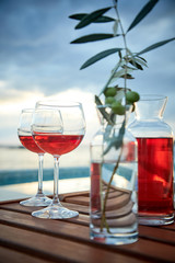 two glasses of rose wine with  olives against blue water on a pier..