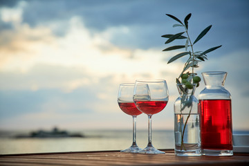 two glasses of rose wine with  olives against blue water on a pier..