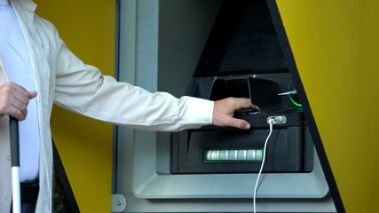 Visually impaired man inserting password on atm machine, withdrawing money